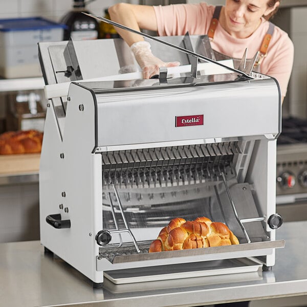 A woman using an Estella countertop bread slicer to slice bread.