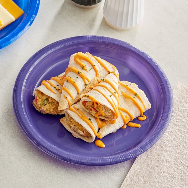 A close up of a Creative Converting purple plastic plate with two burritos and cheese sauce on it.