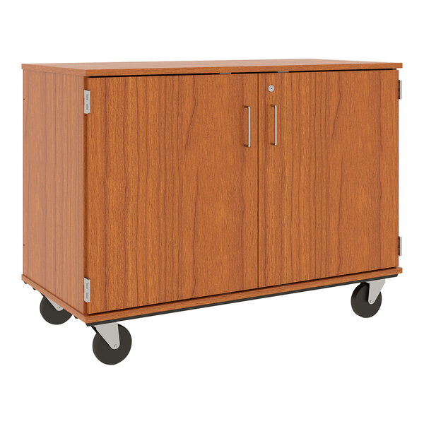A medium cherry wooden cabinet on wheels with slotted storage and a locking door.