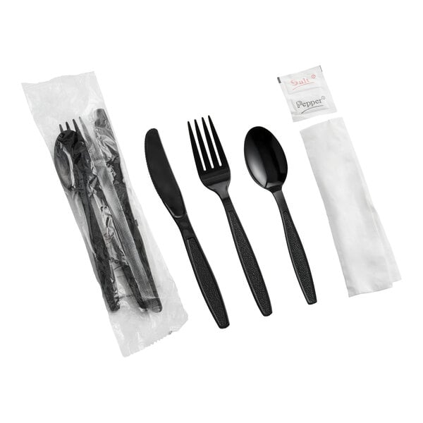 A wrapped cutlery kit containing a black plastic fork, knife, spoon, napkin, and packets of salt and pepper.