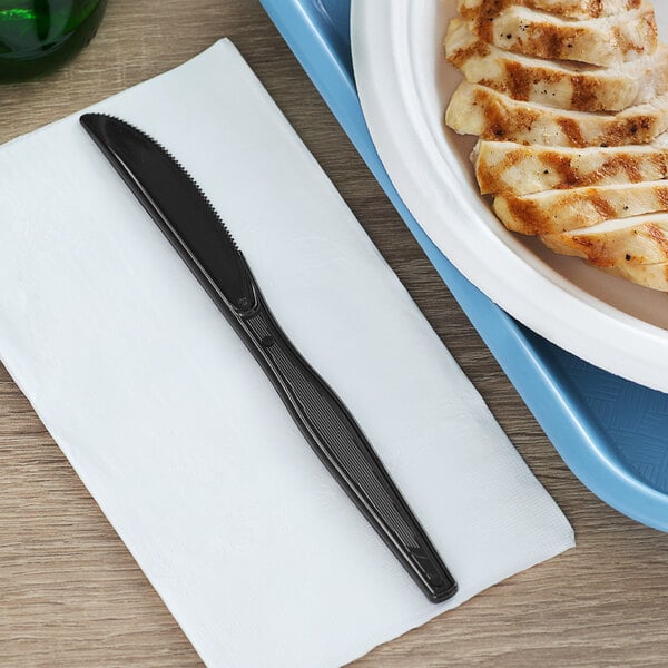 A plate of chicken with a Dixie black polystyrene knife on a table.