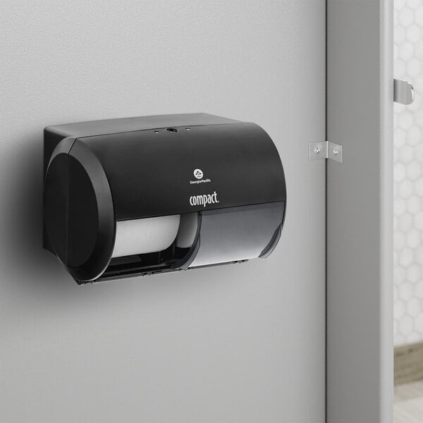 A black Compact by GP Pro double coreless roll toilet paper dispenser on a wall.