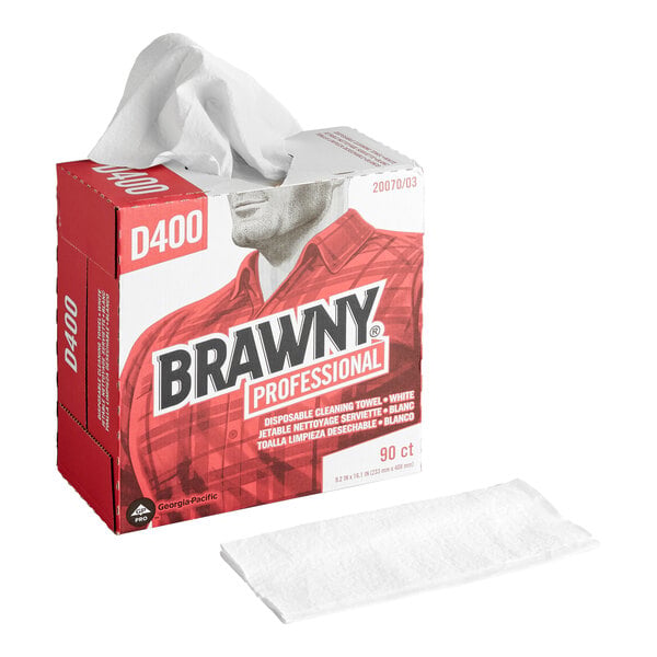 A red and white box labeled 'Brawny Professional' dispenses a white disposable cleaning towel, with one towel also shown lying flat in front of the box.
