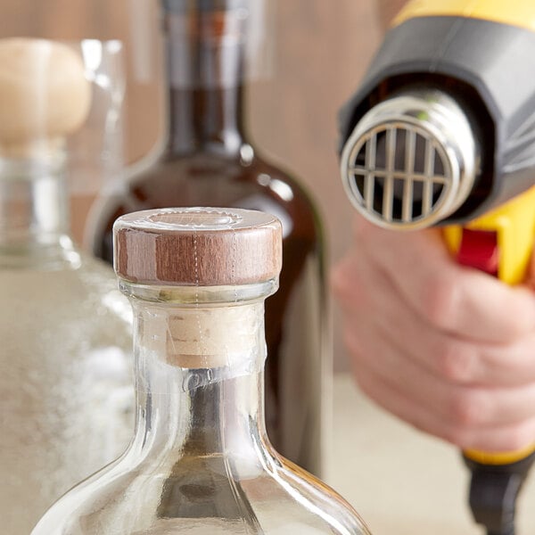 A hand using a blow dryer to shrink a clear perforated shrink band on a bottle.