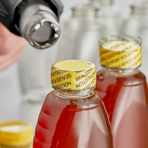 A close-up of a person using a 1" non-perforated shrink band to seal a bottle of liquid.