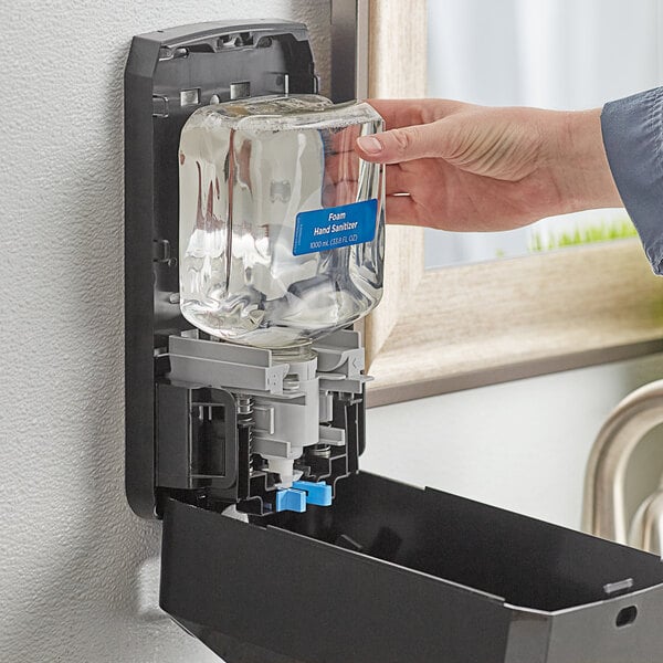 A hand using a Pacific Blue Ultra foam hand sanitizer refill to fill a dispenser.