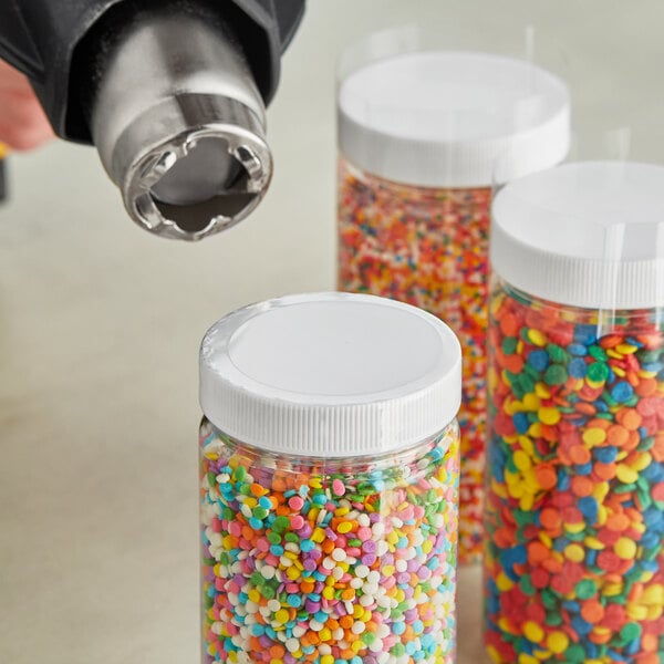 A group of plastic containers with colorful sprinkles over a jar with a clear shrink band on it.