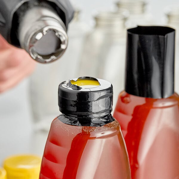 A person using a black shrink band to seal a bottle.