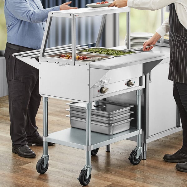 A group of people standing around a ServIt commercial steam table with a sneeze guard.