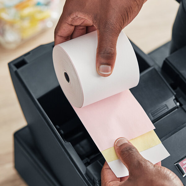 A hand holding a PointPlus carbonless paper roll.