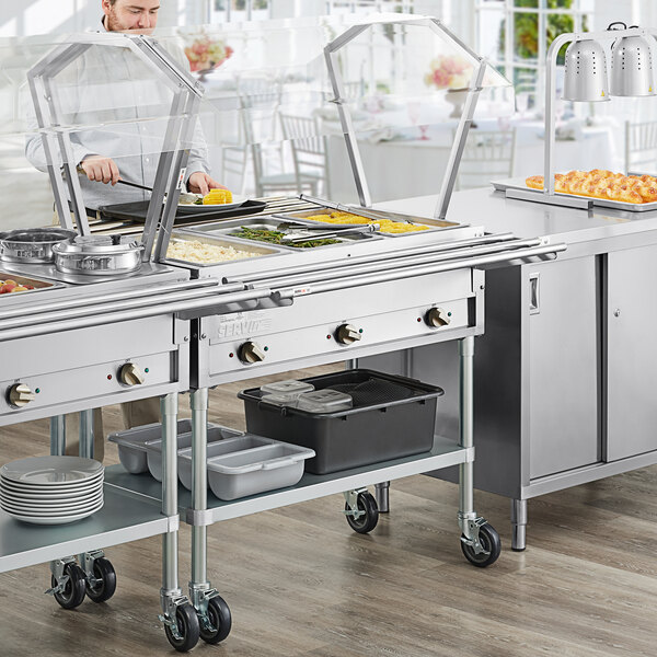 A man in a kitchen preparing food on a ServIt steam table with sneeze guard.