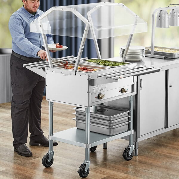 A man in a blue shirt and black pants standing next to a ServIt steam table with food.