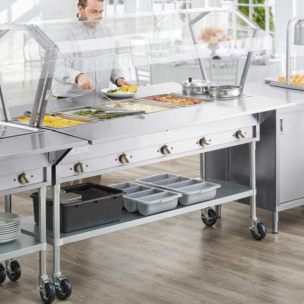 A man using a ServIt electric steam table with a glass sneeze guard.