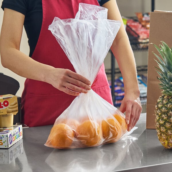A person holding a clear plastic produce bag filled with oranges on a countertop.