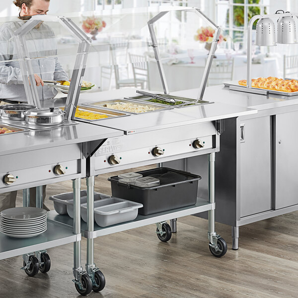 A man in a white coat using a ServIt open well steam table with sneeze guards.