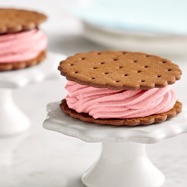 Two cookies with pink ice cream in the middle on a white surface.