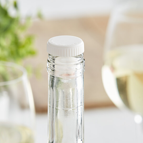 A bottle of white wine with a Franmara white plastic wine pourer/stopper on a table.