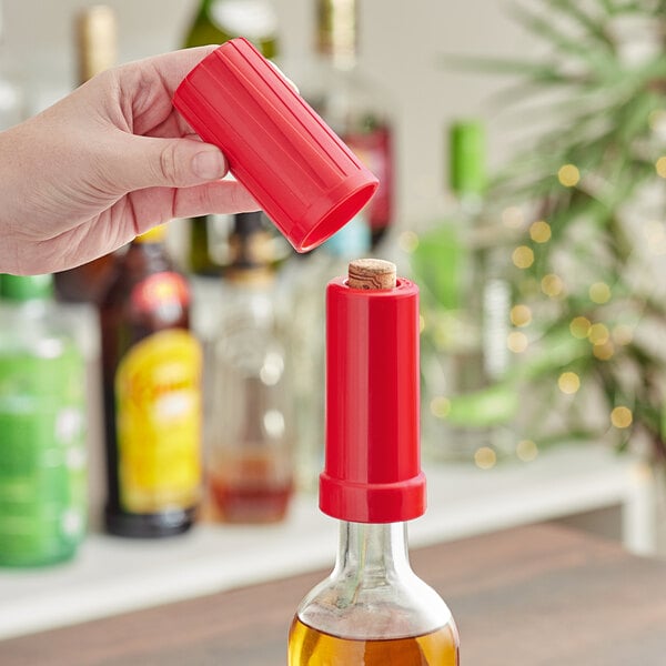 A hand using a Franmara red plastic wine recorker to seal a bottle of wine.