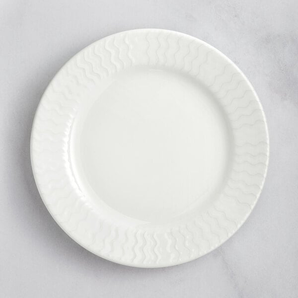 A close up of a white RAK Porcelain flat plate with wavy lines on the rim.