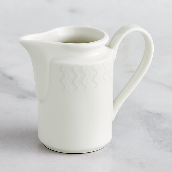 A RAK Porcelain Leon ivory porcelain creamer with a handle on a marble surface.