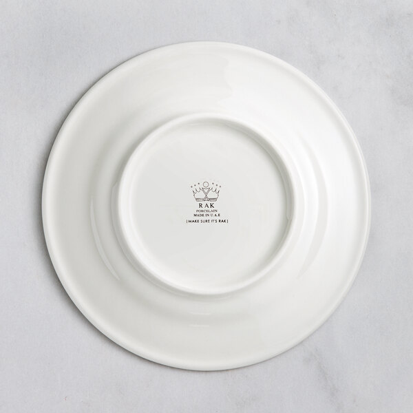 A white RAK Porcelain flat plate with an embossed crown logo on the rim.