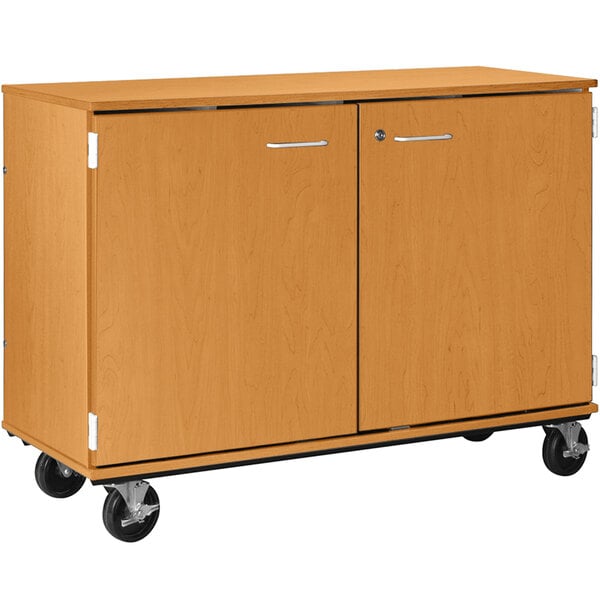 A light oak wooden cabinet on wheels with locking doors.