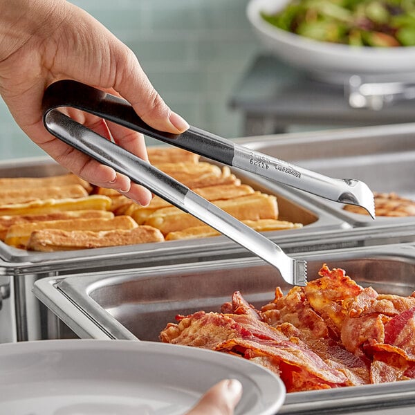 A person holding Vollrath Kool-Touch tongs to a tray of food.