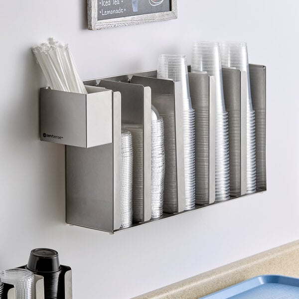 A stainless steel wall-mounted or countertop holder with five sections for cups and lids and an attached straw caddy.