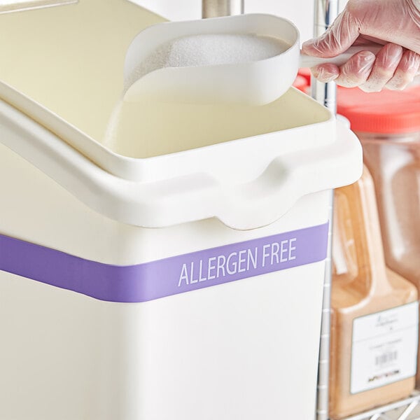 A person in plastic gloves using a Baker's Mark silicone band to pour sugar into a white container.