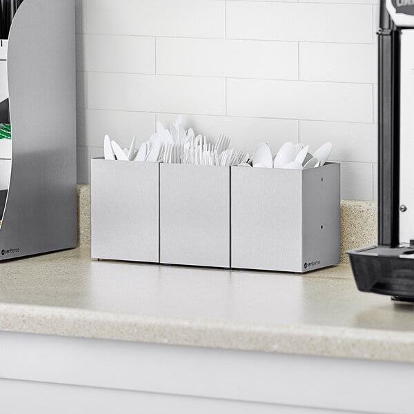 A ServSense stainless steel 3-section flatware organizer on a kitchen counter full of utensils.