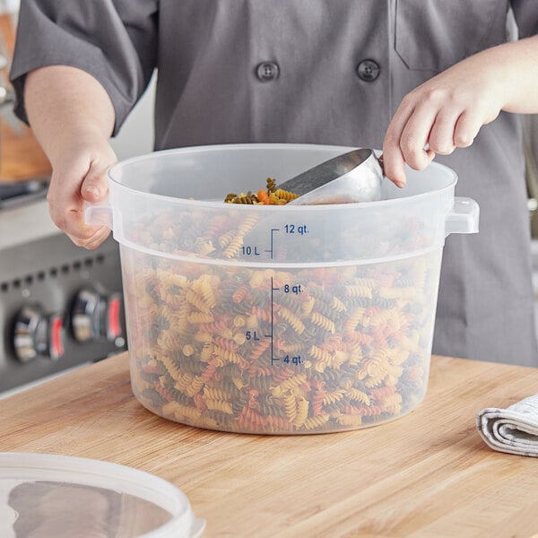 A person using a ladle to put pasta in a plastic container.