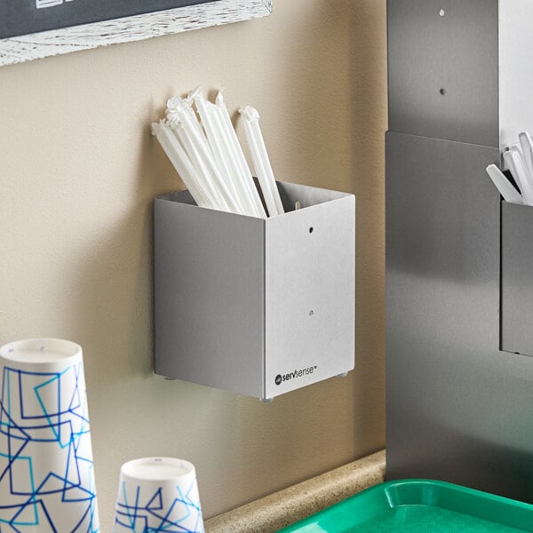 A stainless steel countertop or wall-mount organizer holding wrapped straws.