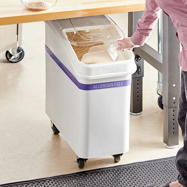 A woman using a scoop to fill a Baker's Lane ingredient bin on a table in a school kitchen.