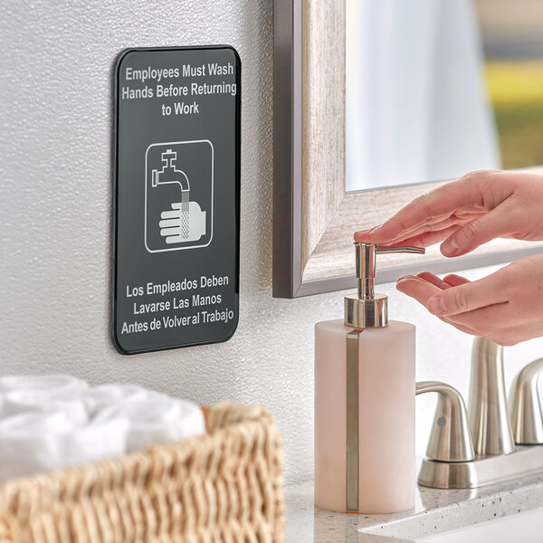 A person using a Tablecraft "Employees Must Wash Hands" sign in a bathroom.