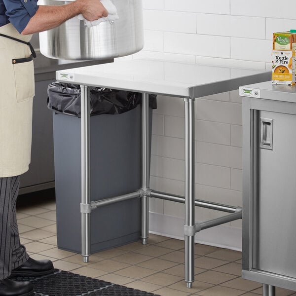 A man in a white apron standing next to a Regency stainless steel work table.