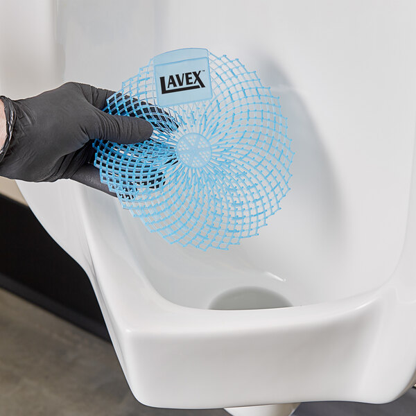 A hand in a black glove holding a blue Lavex Fresh Scented urinal screen.