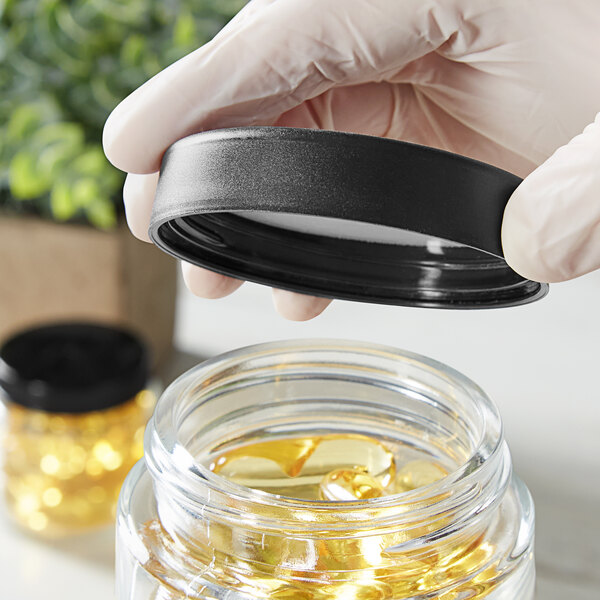 A hand in gloves holding a black Child-Resistant cap over a jar.