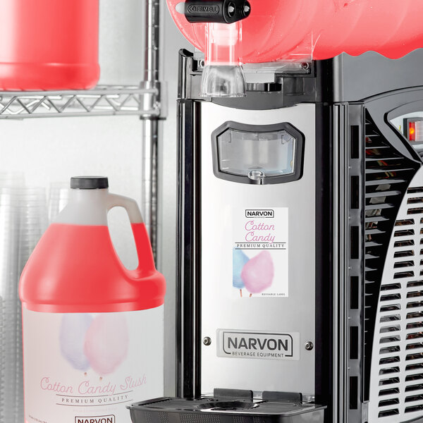 A white and red slushy machine with a red Narvon Cotton Candy concentrate container next to it.