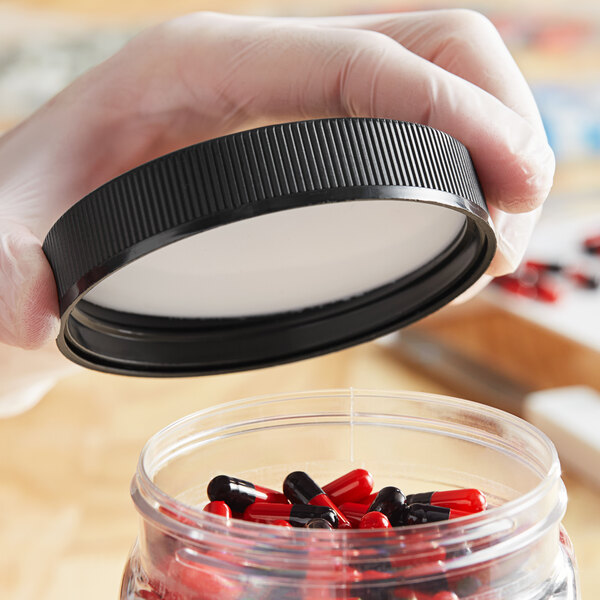 A person in gloves holding a black child-resistant cap over a container of pills.