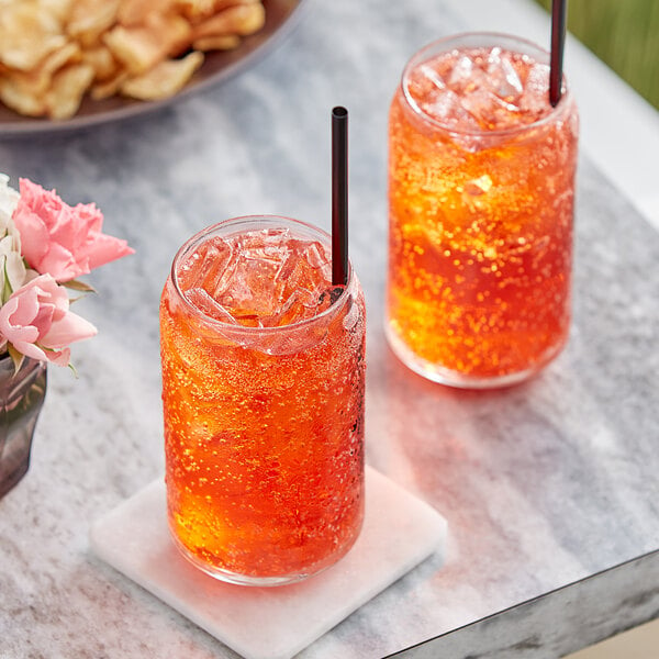 A bag in box of Pure Craft Beverages strawberry soda on a table with two glasses of strawberry soda with ice and straws.