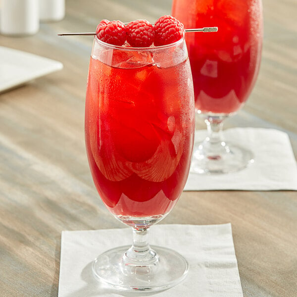 Two glasses of Pure Craft Beverages Raspberry Hibiscus Tea with red liquid and raspberries.