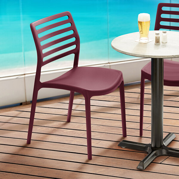 Two red Lancaster Table & Seating Allegro Sangria stackable resin chairs on an outdoor patio overlooking the ocean.