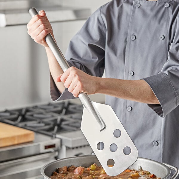 A person using a Fourt&#233; stainless steel paddle over a pot of food.