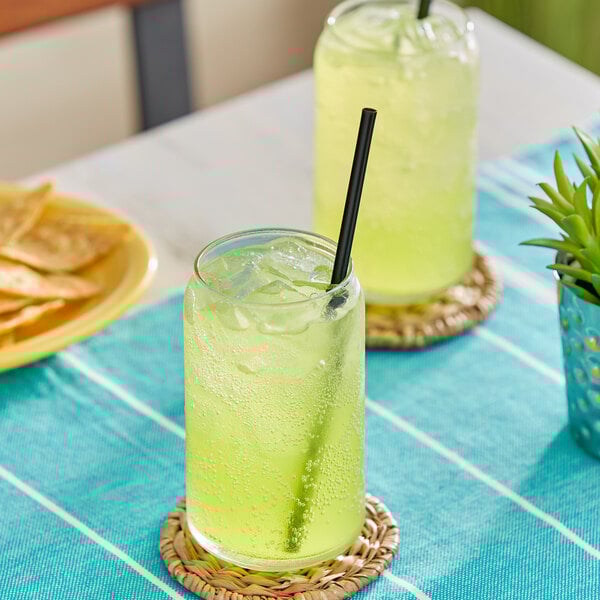 Two glasses of Jarritos Lime soda with straws on a table.