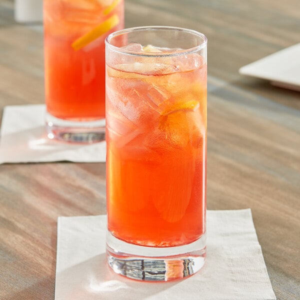 A glass of red liquid with orange liquid and ice on a table.