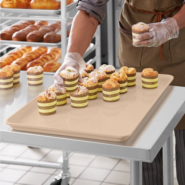 A person in gloves holding a MFG Tray of pastries on a counter in a bakery display.