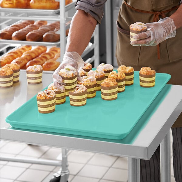 A person in gloves holding a MFG Tray of cupcakes on a green surface.
