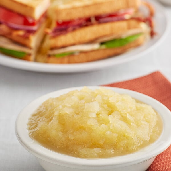 A bowl of Musselman's apple sauce on a table with sandwiches.