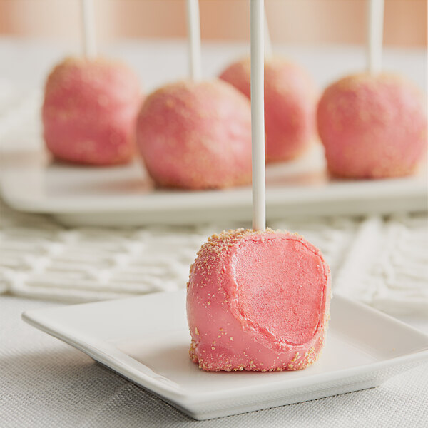 A pink Chalet Desserts strawberry shortcake cake pop on a white stick on a white plate.