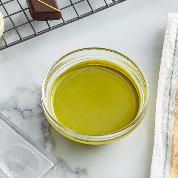 A bowl of green liquid next to a tray of chocolate on a white surface.